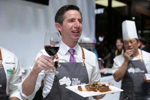 Trade, Tourism and Investment Minister Simon Birmingham holding a glass of red win and plate of food, surrounded by chefs at a cooking demonstration.